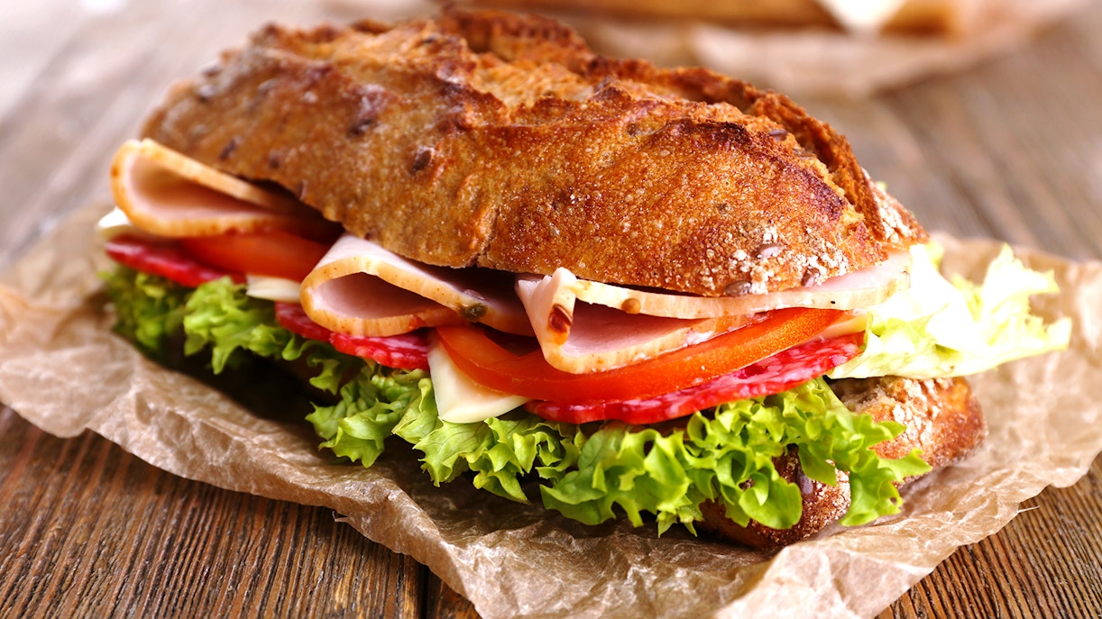 Baguette sandwich with ham, cheese, lettuce, and tomato on a wooden table in Barcelona.