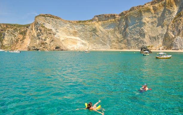 Swimmers enjoying the clear waters near cliffs on Ponza Island during a day trip from Rome.