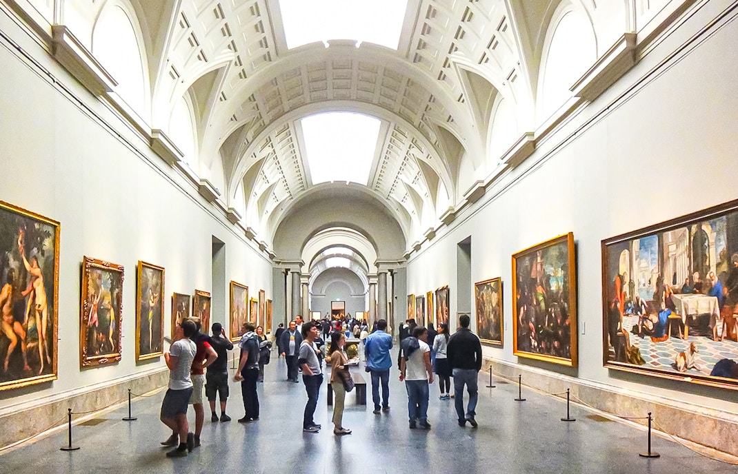 Visitors exploring art exhibits inside the Prado Museum, Madrid, during a guided tour.