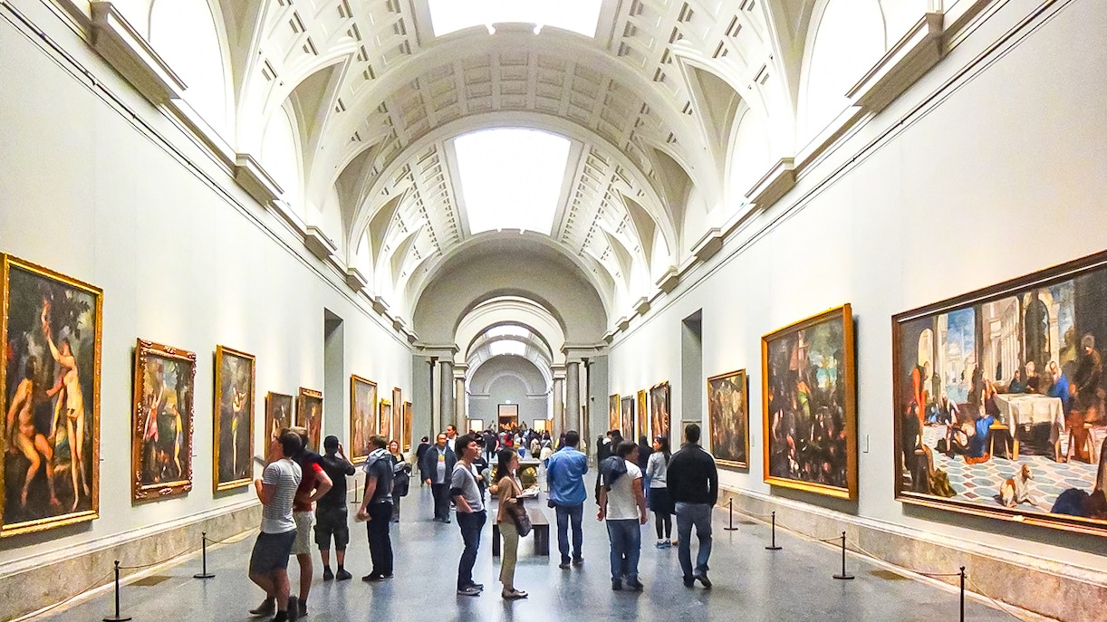 Visitors exploring art exhibits inside the Prado Museum, Madrid, during a guided tour.