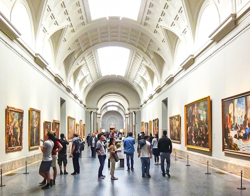Visitors exploring art exhibits inside the Prado Museum, Madrid, during a guided tour.