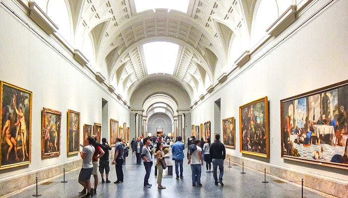 Visitors exploring art exhibits inside the Prado Museum, Madrid, during a guided tour.