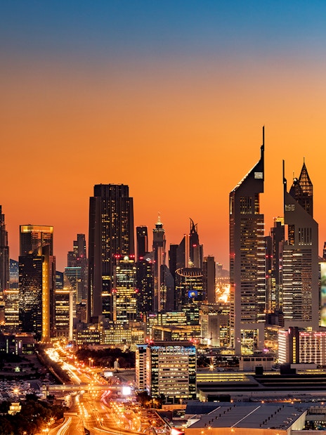 Dubai skyline at sunset featuring Burj Khalifa and illuminated skyscrapers.