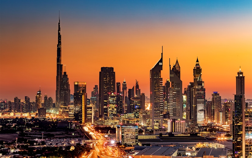 Dubai skyline at sunset featuring Burj Khalifa and illuminated skyscrapers.