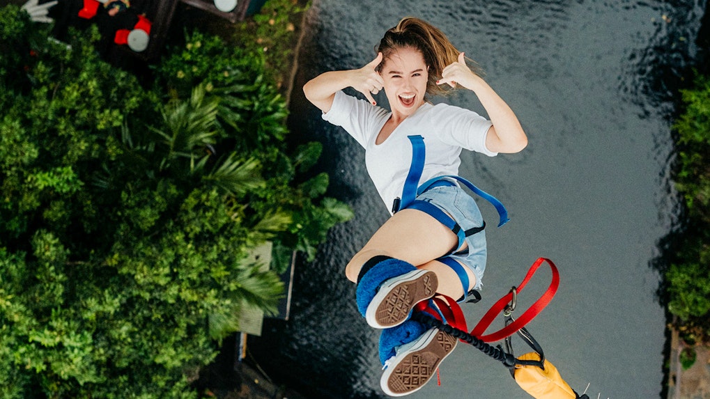 Bungee jumper mid-air at Skypark Cairns over lush greenery and water.