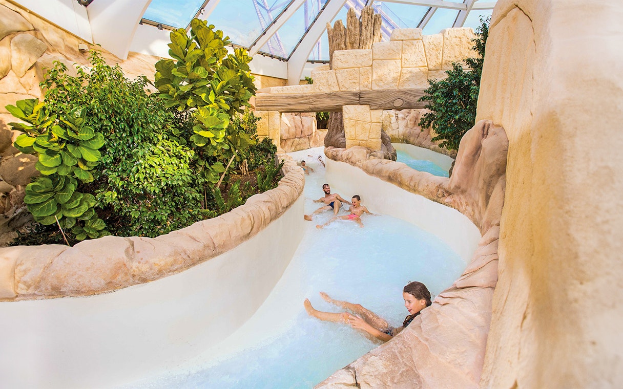 Tourists sliding down the Rapido slide at Aqualibi, surrounded by lush greenery.