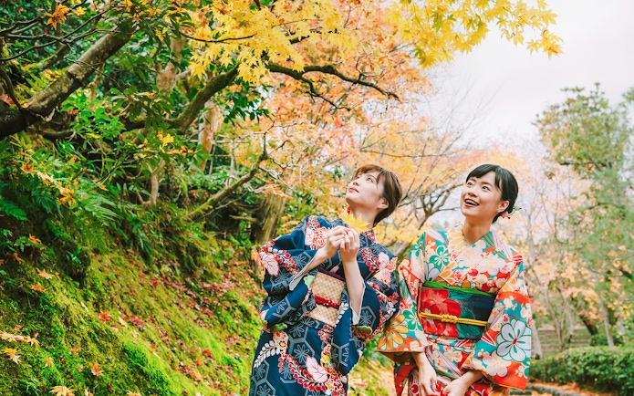 Friends in colorful kimonos enjoying autumn foliage in a Japanese garden.