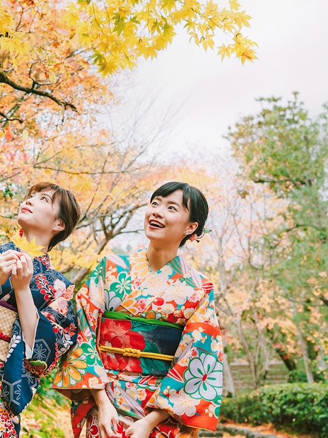 Friends in colorful kimonos enjoying autumn foliage in a Japanese garden.