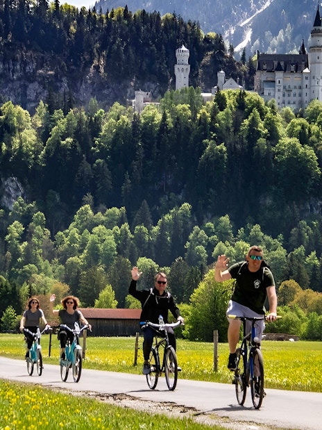 Cyclists on a path with Neuschwanstein Castle in the background, summer tour from Munich.