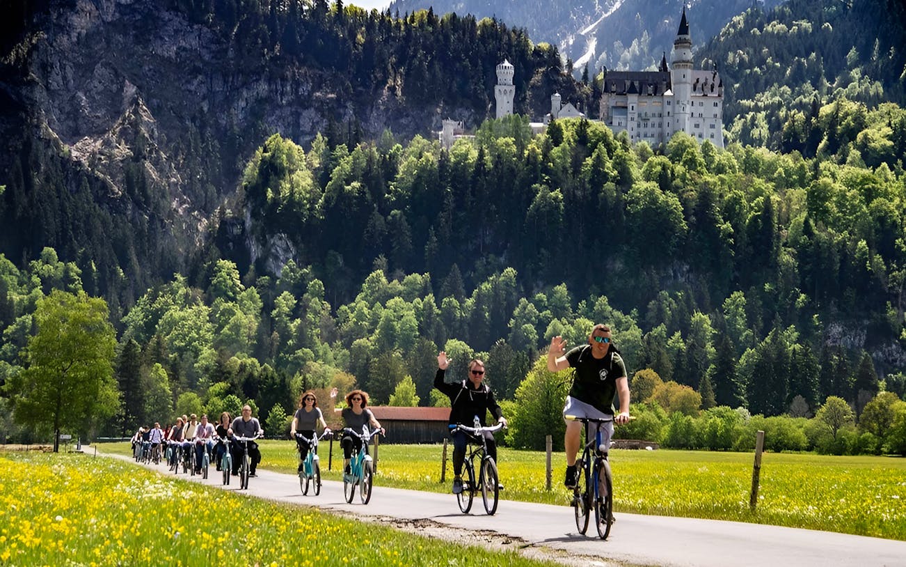 Cyclists on a path with Neuschwanstein Castle in the background, summer tour from Munich.