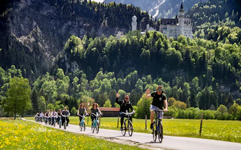 Cyclists on a path with Neuschwanstein Castle in the background, summer tour from Munich.