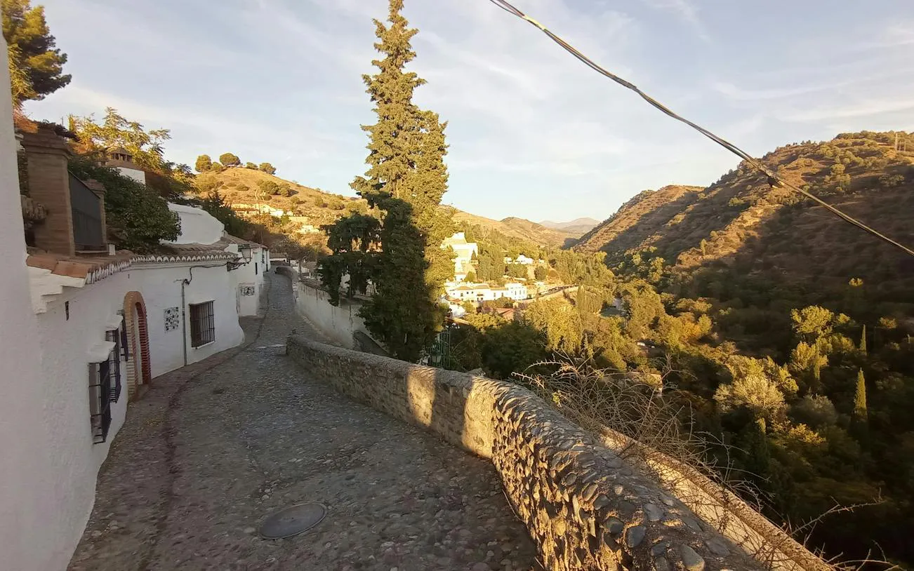 Cobblestone path in Sacromonte, Granada, with hillside views and traditional white houses.