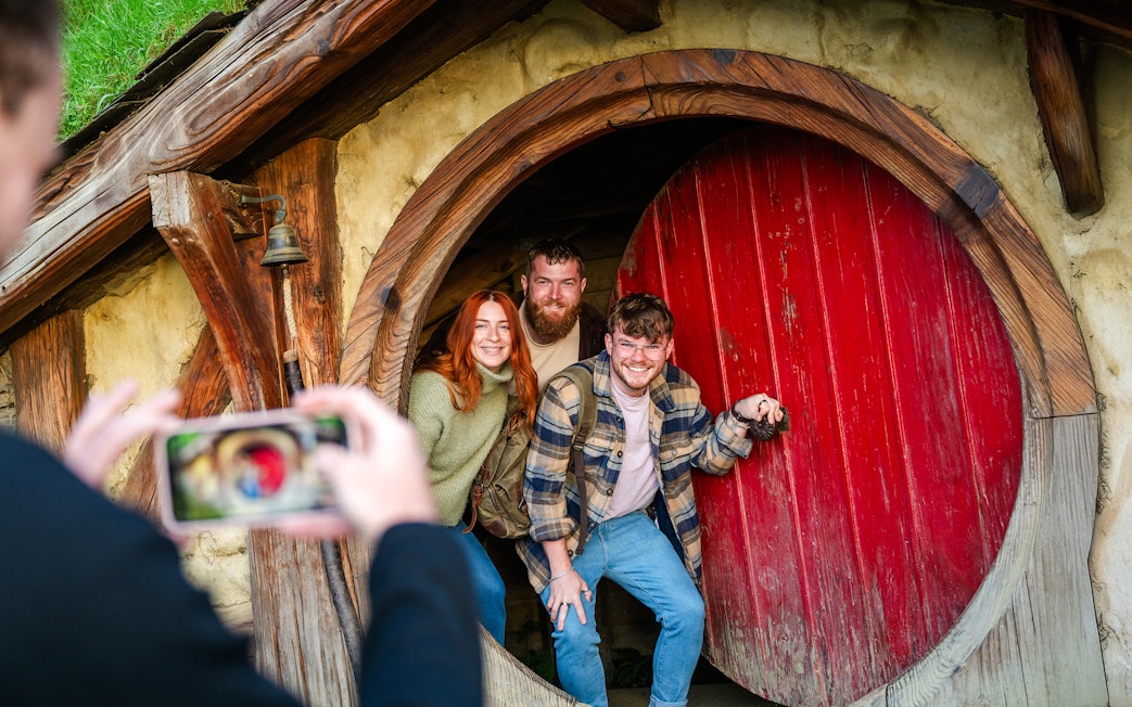 Friends posing at the round door of a hobbit house, Hobbiton movie set tour.