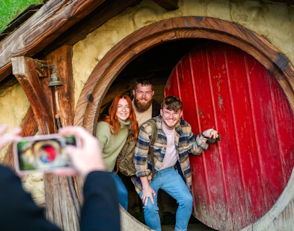 Friends posing at the round door of a hobbit house, Hobbiton movie set tour.