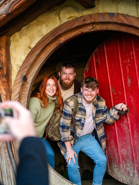Friends posing at the round door of a hobbit house, Hobbiton movie set tour.