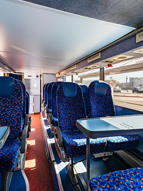 Interior of a bus with blue seats and tables, route Bergamo Airport to Milan Centrale.