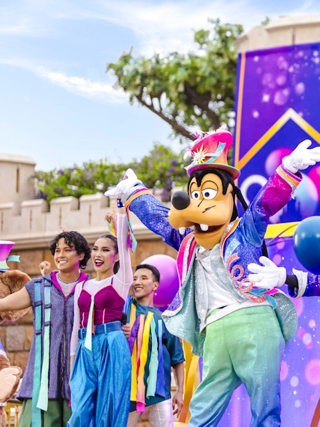 Disney characters in a parade at Disneyland Hong Kong with colorful costumes and castle backdrop.