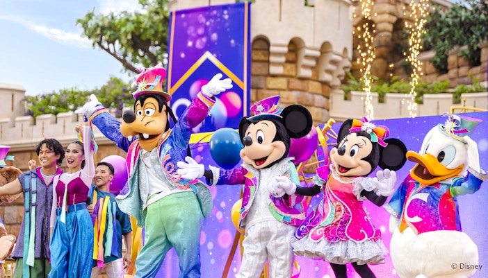 Disney characters in a parade at Disneyland Hong Kong with colorful costumes and castle backdrop.