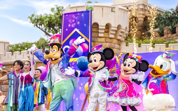 Disney characters in a parade at Disneyland Hong Kong with colorful costumes and castle backdrop.