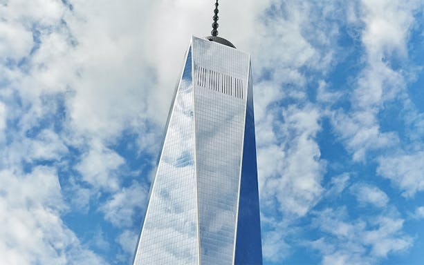 One World Trade Center tower against a cloudy blue sky in New York City.