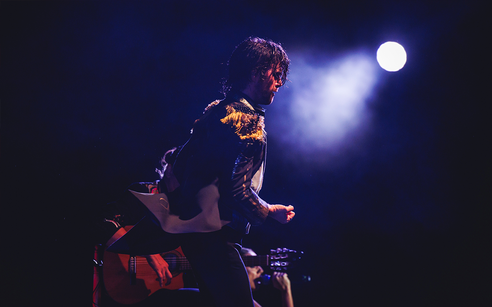 Performer on stage with guitar under spotlight, WAH tour.