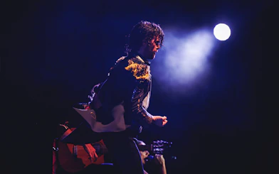 Performer on stage with guitar under spotlight, WAH tour.