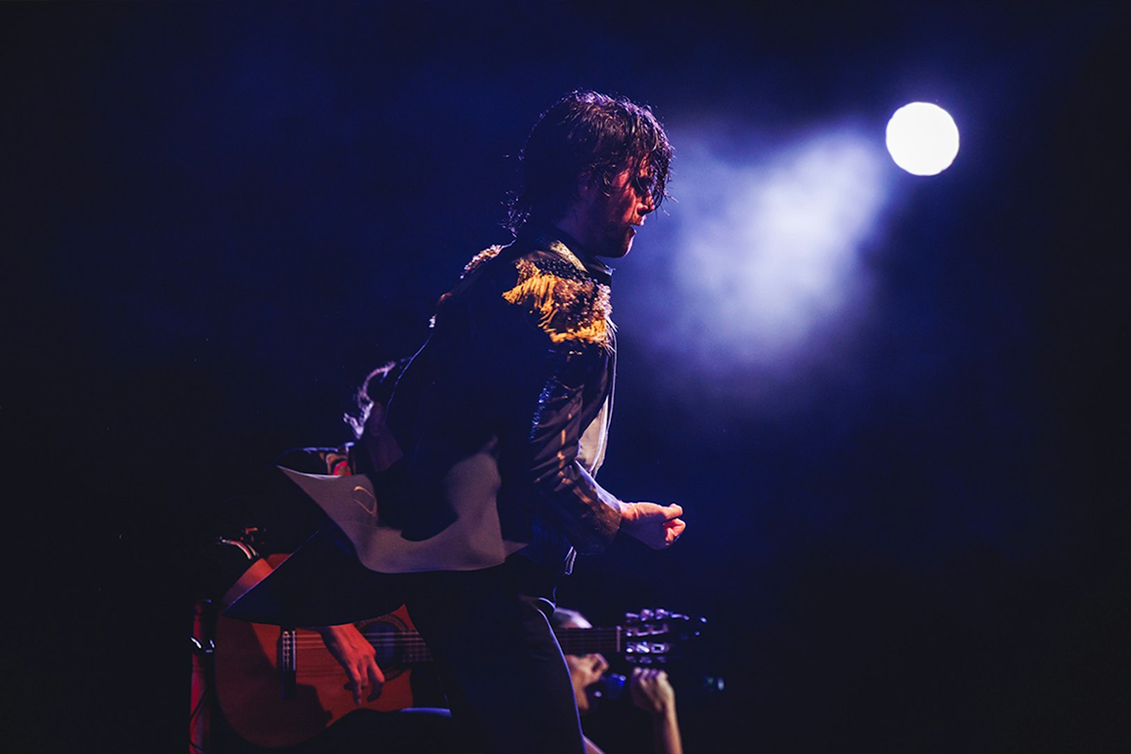 Performer on stage with guitar under spotlight, WAH tour.