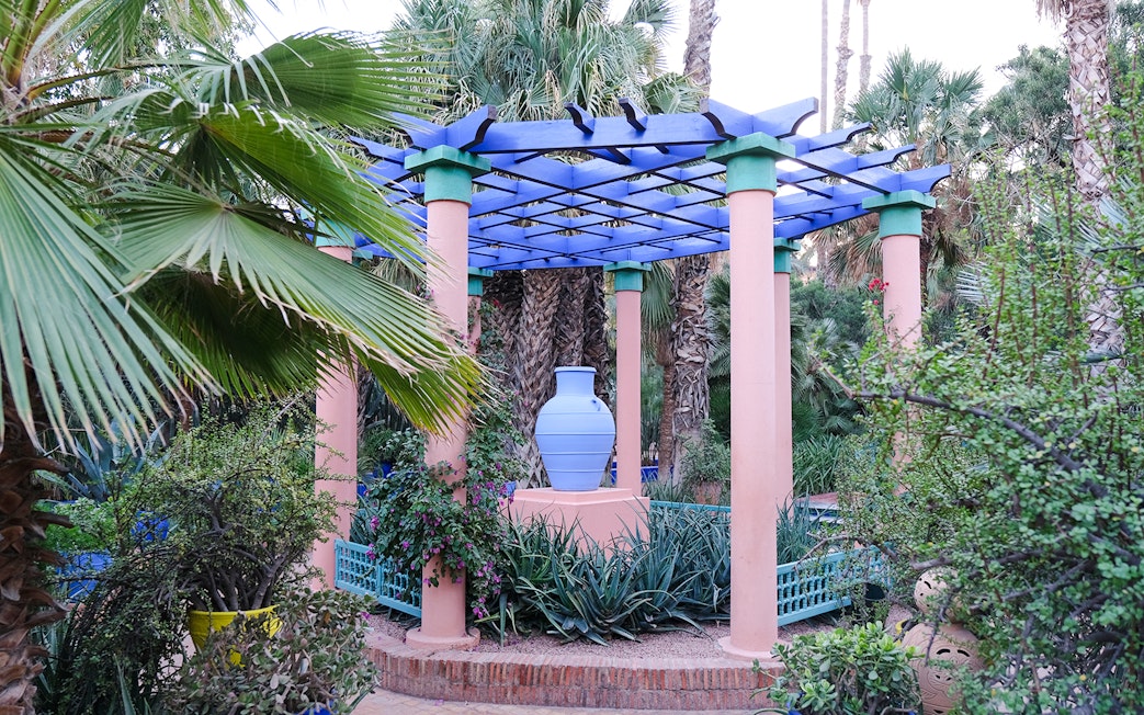 Pergola with blue vase surrounded by lush plants in Jardin Majorelle, Marrakech.