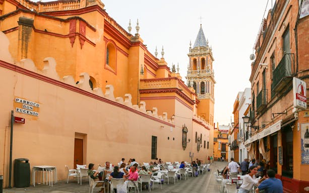 Outdoor dining in Triana, Seville, with view of historic church tower.