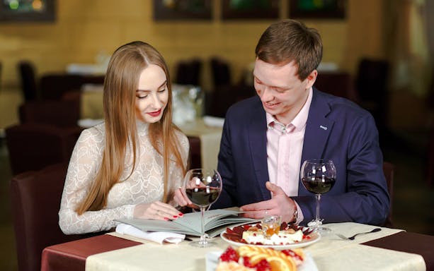 Couple reviewing menu on a cruise dining table with wine and dessert.
