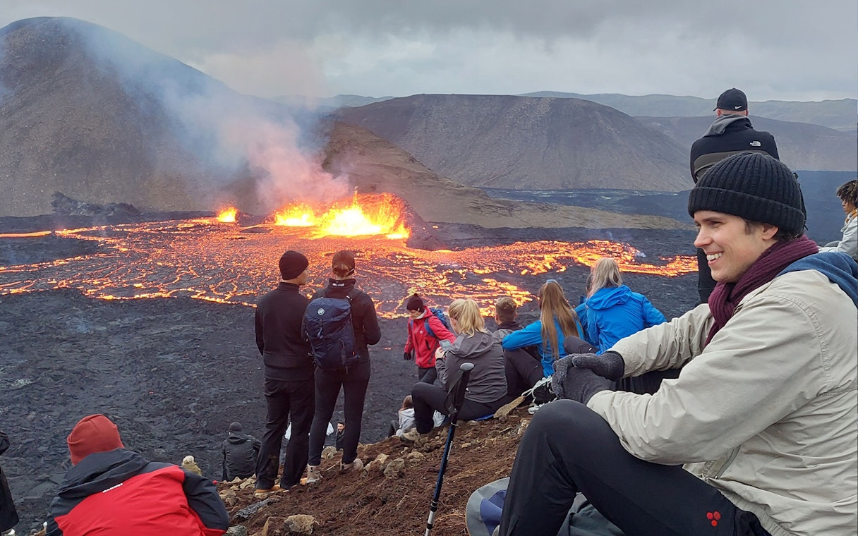 Tourists observing volcanic eruption at Reykjanes, Iceland, with visible lava flow.