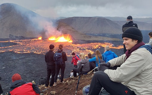 Tourists observing volcanic eruption at Reykjanes, Iceland, with visible lava flow.
