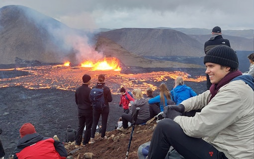 Tourists observing volcanic eruption at Reykjanes, Iceland, with visible lava flow.