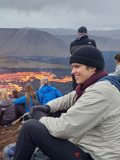 Tourists observing volcanic eruption at Reykjanes, Iceland, with visible lava flow.