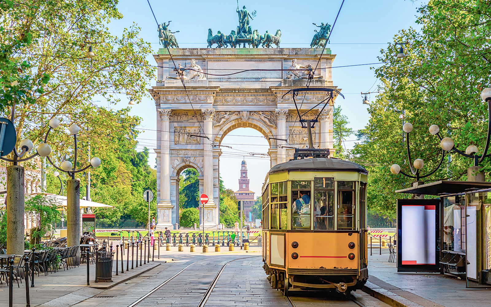 Milan vintage tram passing by Arco della Pace in a tree-lined street.