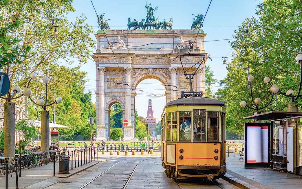 Milan vintage tram passing by Arco della Pace in a tree-lined street.
