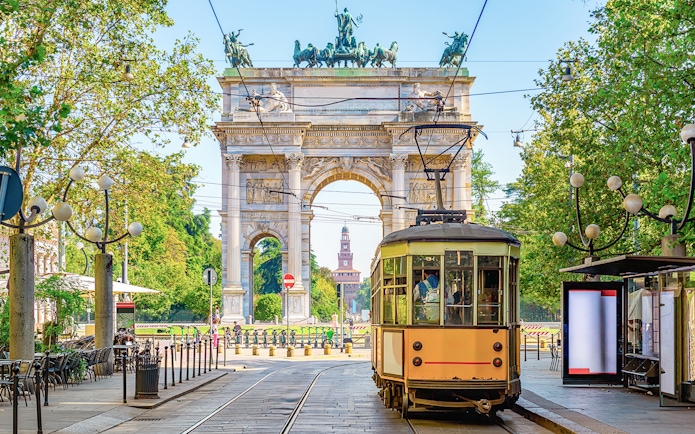 Milan vintage tram passing by Arco della Pace in a tree-lined street.