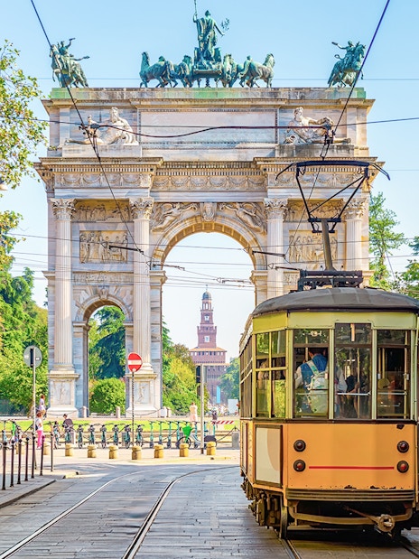 Milan vintage tram passing by Arco della Pace in a tree-lined street.