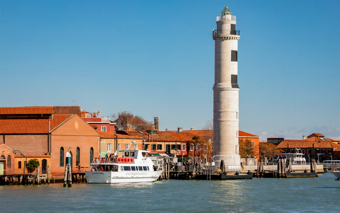 Ferry near Murano lighthouse in Venice, Italy, with colorful buildings in the background.