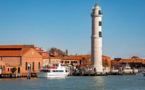 Ferry near Murano lighthouse in Venice, Italy, with colorful buildings in the background.