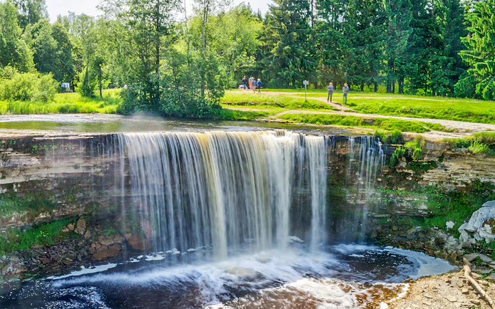 Jagala Waterfall cascading over rocks in a lush green forest, Northern Estonia.