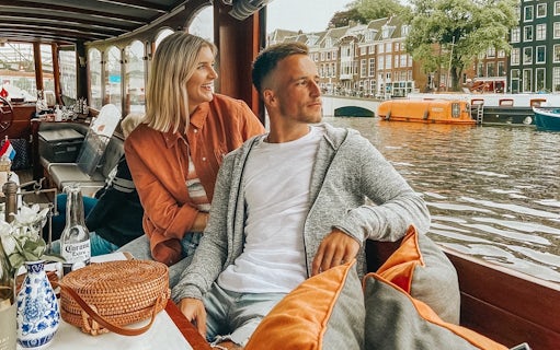 Couple enjoying a canal cruise in Amsterdam with historic buildings in the background.