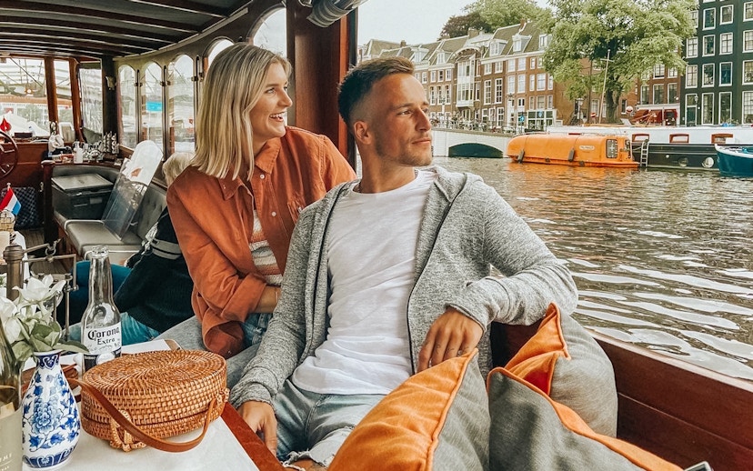 Couple enjoying a canal cruise in Amsterdam with historic buildings in the background.