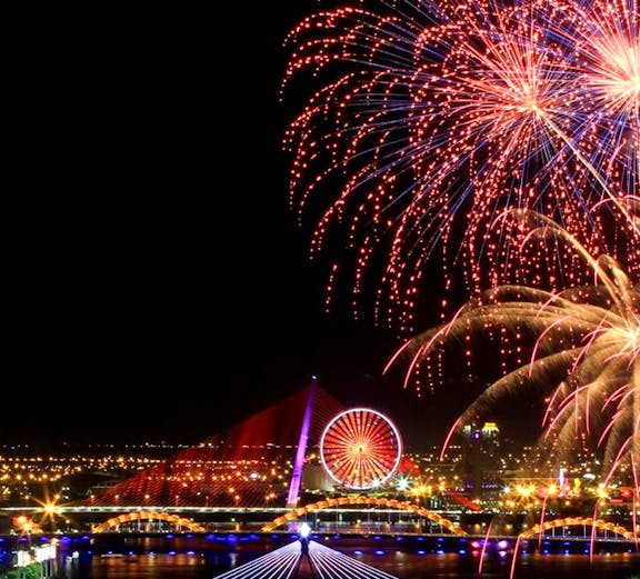 Fireworks over Da Nang skyline with bridges and Ferris wheel during festival.
