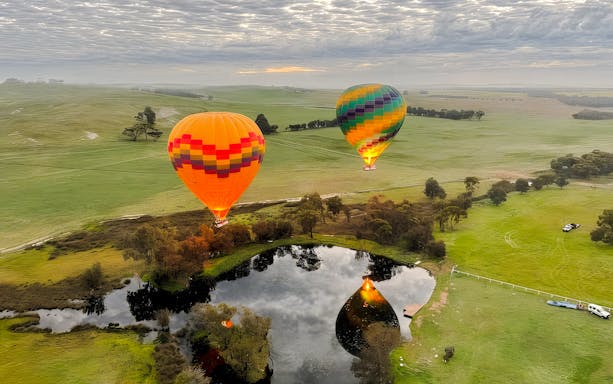 Aerial view of hot air balloons over Avon Valley landscape with reflection in a pond.