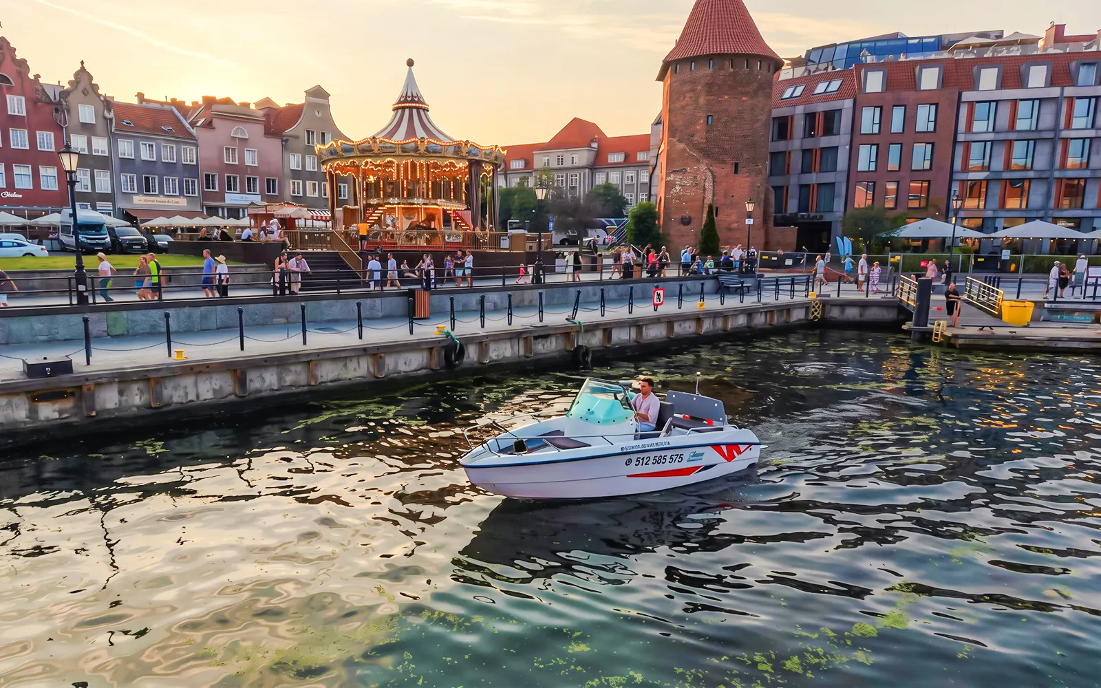 Electric boat on Gdansk harbour during Motława Sunset Cruise with historic buildings in background.