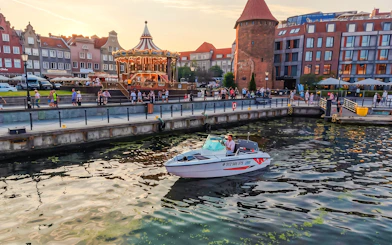 Electric boat on Gdansk harbour during Motława Sunset Cruise with historic buildings in background.