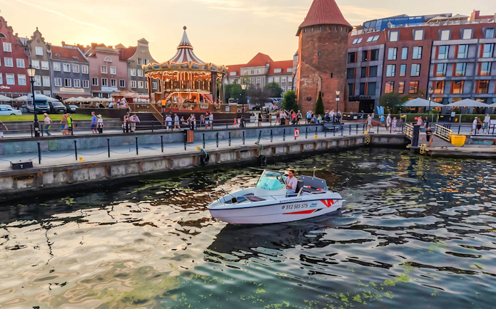 Electric boat on Gdansk harbour during Motława Sunset Cruise with historic buildings in background.
