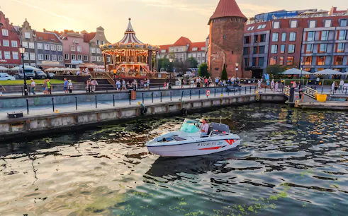 Electric boat on Gdansk harbour during Motława Sunset Cruise with historic buildings in background.