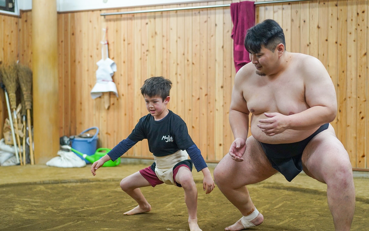 Child practicing sumo wrestling with a sumo wrestler in Tokyo dojo.